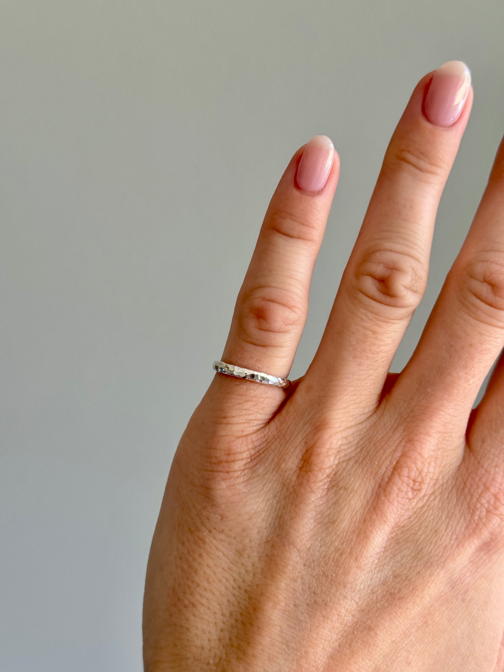 Hand wearing a silver pinky ring on a neutral background